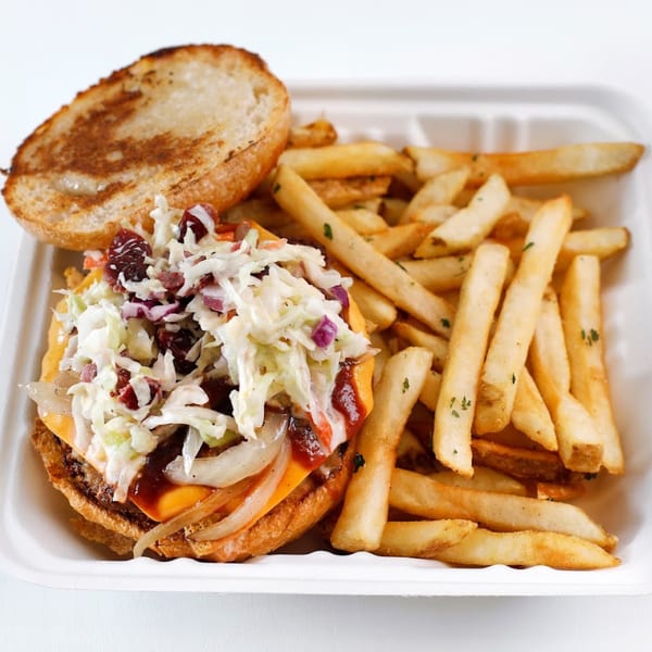 Vegan Mob's vegan BBQ burger with coleslaw, onions, and fries in a white to-go container.