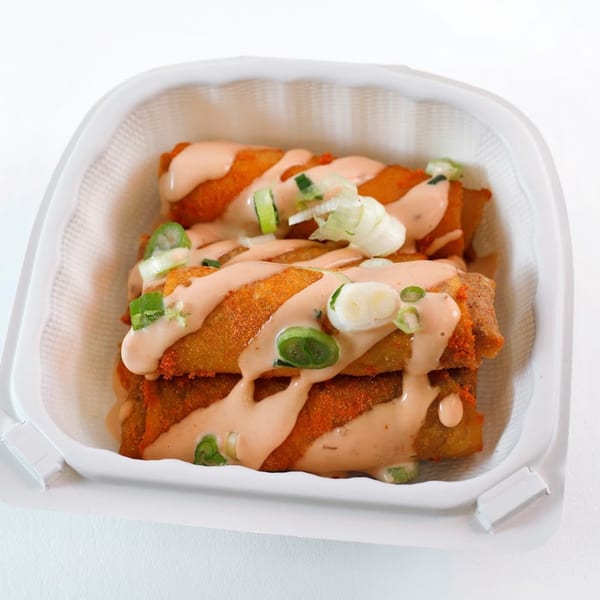 Vegan Mob's crispy vegan egg rolls drizzled with creamy sauce and topped with green onions.